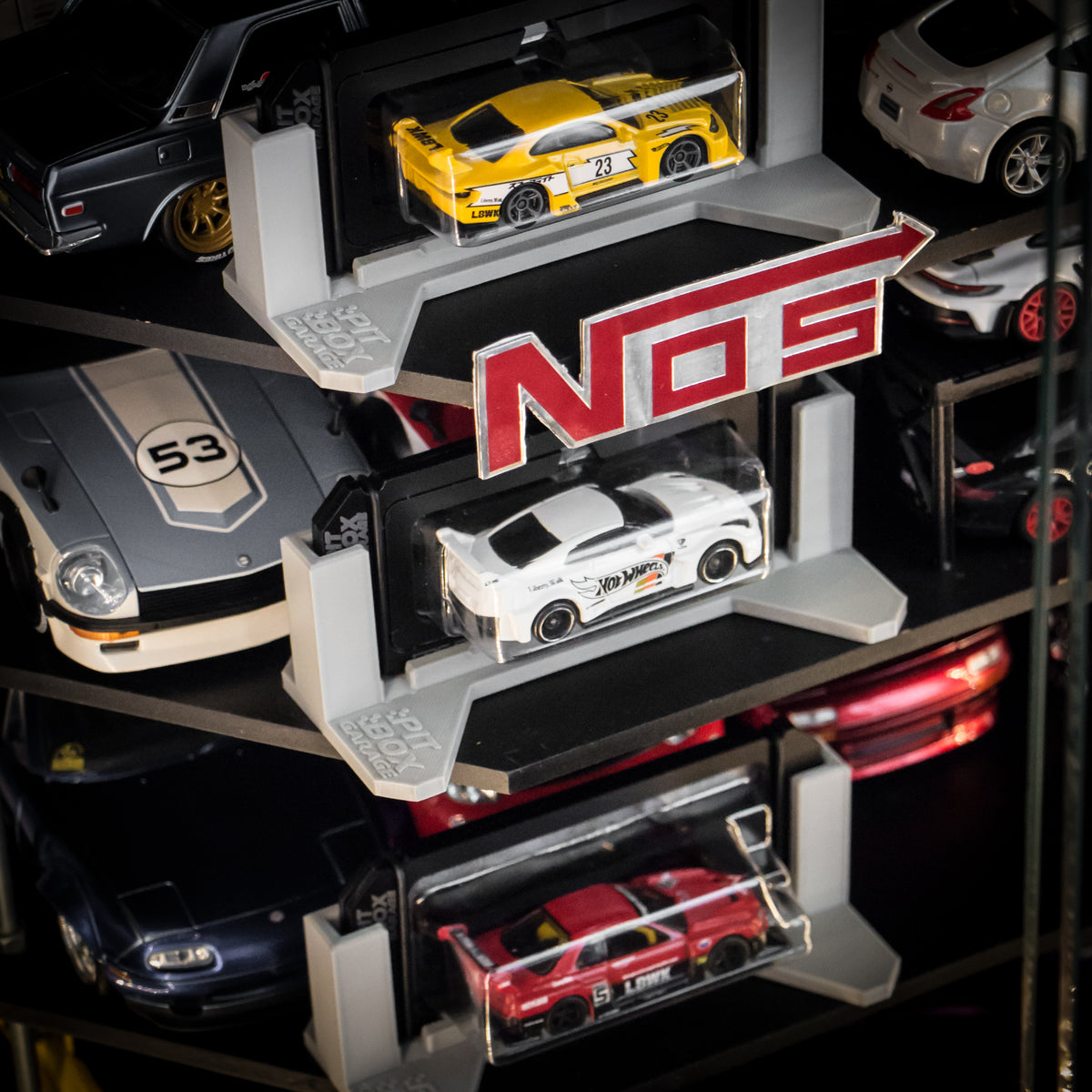 A close-up of a multi-tiered NOS display shelf holding several die-cast model cars, including a yellow race car, a white sports car, a red car, and other cars partially visible on the shelves.