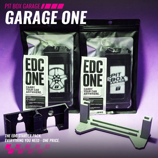 Pit Box Garage Garage One EDC Starter Pack shown with two black resealable pouches, a black mounting bracket, and a light gray/white plastic tool on a purple gradient background. Visible branding includes PIT BOX GARAGE and EDC ONE.
